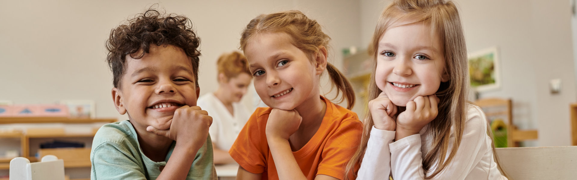 cheerful and multiethnic kids looking at camera near table in class of montessori school