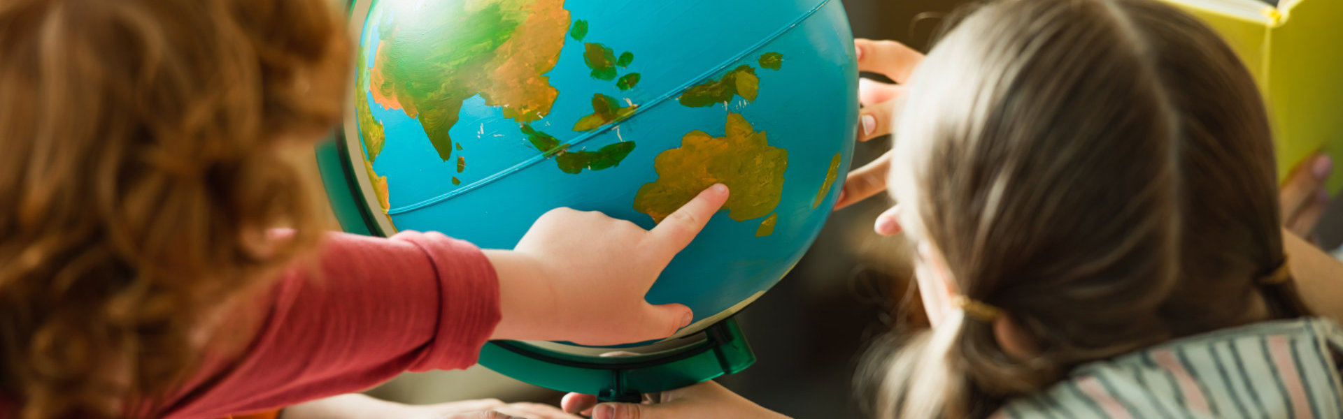 back view of blurred boy pointing at globe near kids and teacher