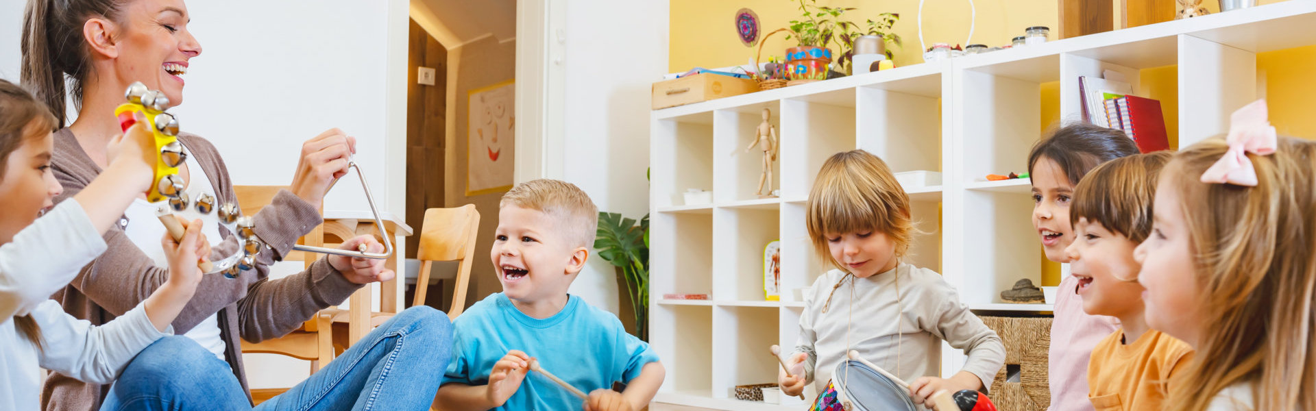 Kindergarten teacher with children sitting on the floor having music class, using various instruments and percussion.